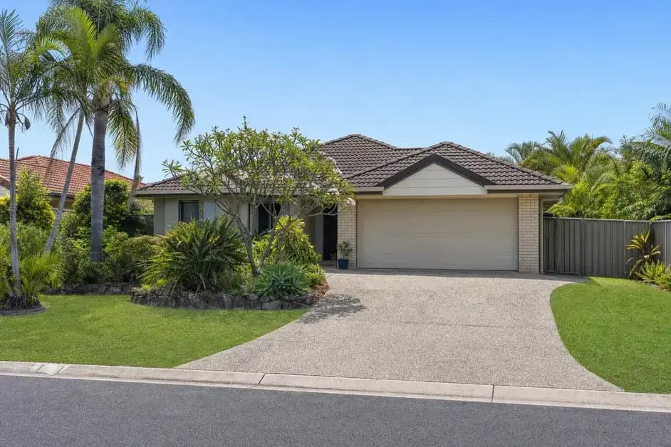 A single-storey rendered and brick Gold Coast home with a tiled hip roof, a wide driveway and established subtropical planting